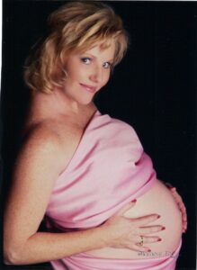 A pregnant woman in pink dress posing for the camera.